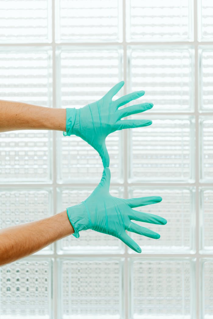 Close-up of two hands in green medical gloves against a glass background.