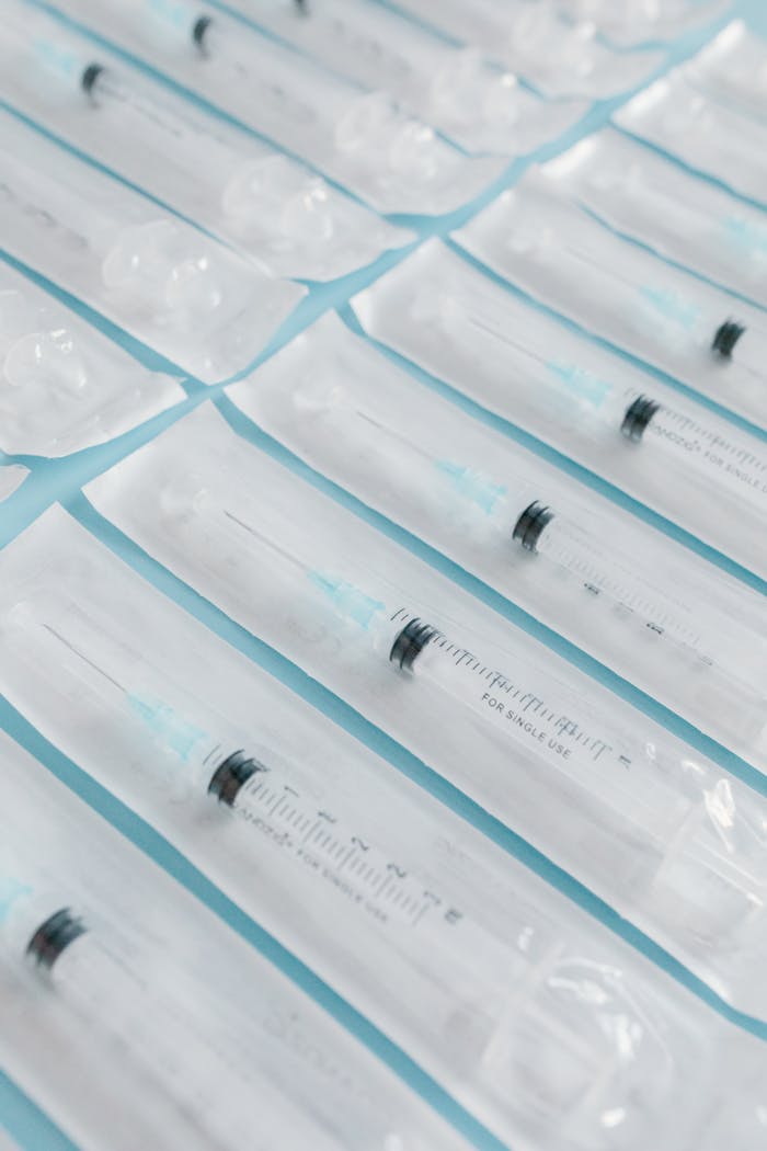 High-angle shot of sterile syringes in individual packaging arranged on a blue surface.