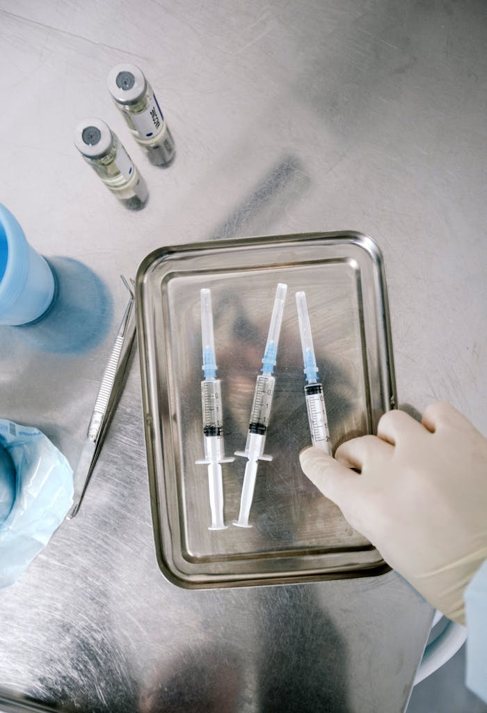 Close-up of sterile syringes and vaccine vials prepared for use on a stainless steel tray.